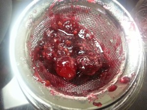 Cranberries getting strained into a pint size mason jar...